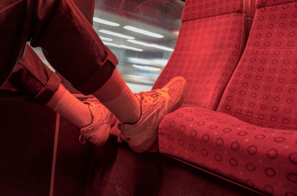 An individual rests his white trainer covered feet on the opposite seat on a bus or train.