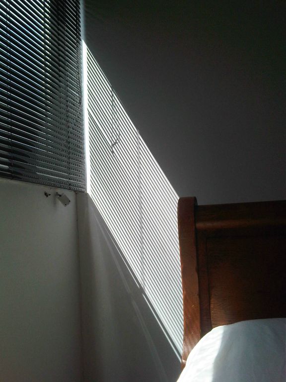 Light shining through black blinds onto the end of a bed.