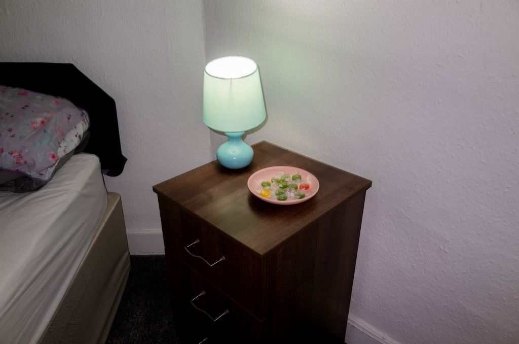 Some brightly coloured boiled sweets lie in a pink plate on a bedside table next to an aquamarine bedside lamp.