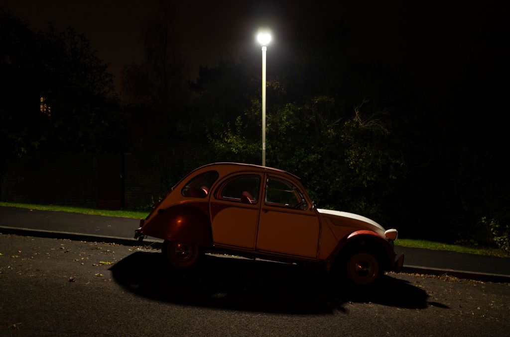 A red and white Citroen Dolly 2cv car depicted at night under streetlight.